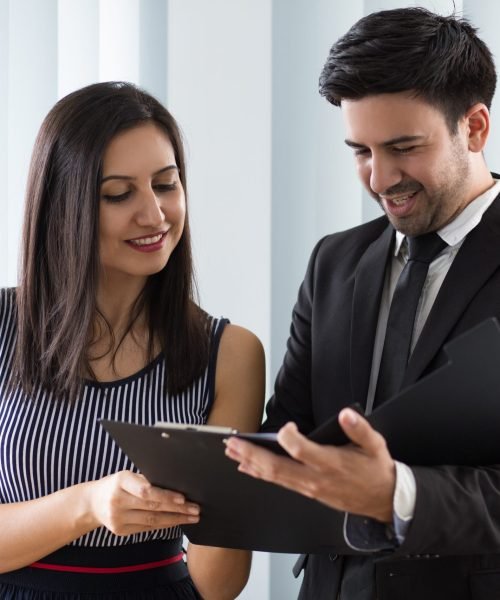 Smiling confident colleagues examining document together. Positive handsome man in suit showing folder with papers while talking to business partner. Cooperation concept